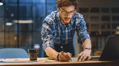 Masasında Çalışan Genç Yaratıcı Tasarımcı, Bir Tasarım, Çizim Konsepti ve Çizimler üzerine yoğunlaşmış. Pencereli Arkaplan Akşam Ofisi Stüdyosunda