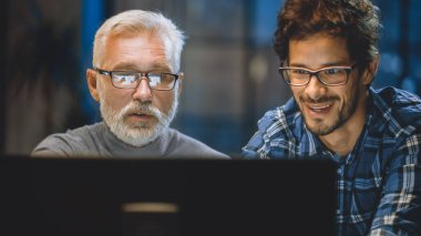 Baş Yaratıcı Tasarımcı Masaüstü Bilgisayar Ekranını Genç Bir Geliştiriciye Gösteriyor, Proje Tartışıyorlar. Tartışan iki profesyonel var. Doğru Tasarım Konsepti Seçimi. Stüdyo ofisinde akşam