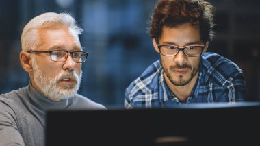 Baş Yaratıcı Tasarımcı Masaüstü Bilgisayar Ekranını Genç Bir Geliştiriciye Gösteriyor, Proje Tartışıyorlar. Tartışan iki profesyonel var. Doğru Tasarım Konsepti Seçimi. Stüdyo ofisinde akşam