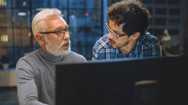 Baş Yaratıcı Tasarımcı Masaüstü Bilgisayar Ekranını Genç Bir Geliştiriciye Gösteriyor, Proje Tartışıyorlar. Tartışan iki profesyonel var. Doğru Tasarım Konsepti Seçimi. Stüdyo ofisinde akşam