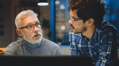 Baş Yaratıcı Tasarımcı Masaüstü Bilgisayar Ekranını Genç Bir Geliştiriciye Gösteriyor, Proje Tartışıyorlar. Tartışan iki profesyonel var. Doğru Tasarım Konsepti Seçimi. Stüdyo ofisinde akşam