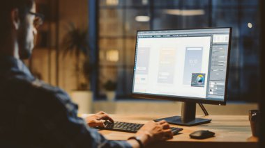 Genç Uygulama Geliştiricisinin Omuz Çekimi Masaüstü Bilgisayarını kullanarak, Yeni Cep Telefonu Uygulama Tasarımı, Yazılım UI Geliştirme Omuzları üzerinde. Şehir Penceresi Görünümlü Modern Ofis Stüdyosunda Akşam