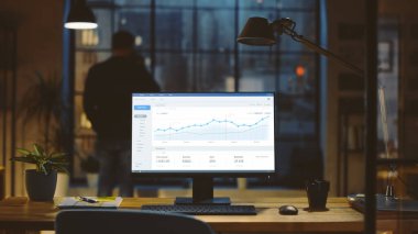 İstatistik Grafiği, Grafik ve Çeşitli Verilerle Bir Masaüstü Bilgisayarı Çekimi, Büyüme ve Başarı Şirketi. Arka planda iş adamı bir kupadan içer Pencereden Gece Şehri 'ne bakar