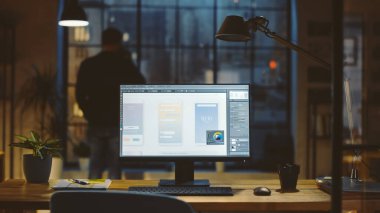 Ofisteki bir Masaüstü Bilgisayarının Çekimi Ekranı Cep Telefonu Uygulama Tasarımı, Yazılım UI Geliştirmesi ile gösterir. Arka planda Tasarımcı Kupadan İçer Pencereden Gece Şehri 'ne bakar.