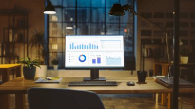 İstatistik Grafiği, Grafik ve Çeşitli Verilerle Bir Masaüstü Bilgisayarı Çekimi, Büyüme ve Başarı Şirketi. Şehir Penceresi Görünümlü Arkaplan Ilık Akşam Işıklandırması ve Açık Uzay Stüdyosunda.