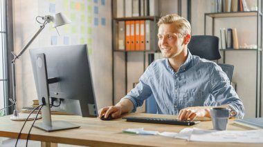 Moda Ofisi 'ndeki Masasında Oturan Yaratıcı Girişimci Masaüstü Bilgisayarı. Yakışıklı Kafkas Adam Bilgisayar Kullanıyor. Modern Minimalizm Tasarımı ile Arka plan Moda Ofis Stüdyosunda