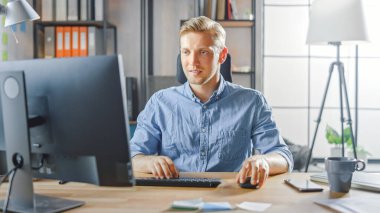 Moda Ofisi 'ndeki Masasında Oturan Yaratıcı Girişimci Masaüstü Bilgisayarı. Yakışıklı Genç İşadamı Bilgisayar Kullanıyor, Dış kaynak kullanıyor, Yeni Uygulamalar Tasarlıyor ve Yazılım Geliştiriyor