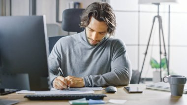 Ofisteki Masasında Masaüstü Bilgisayarında Masasında Oturan Yakışıklı Uzun Saçlı Girişimci, Belgeler, Grafikler, İstatistik ve Şirket Stratejisi ile Çalışıyor. İş Adamı Belgeleri Dolduruyor