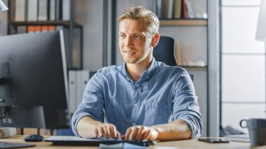 Ofisteki Masasında Masaüstü Bilgisayarında Masasında Oturan Yakışıklı Sarışın Girişimci, Belgeler, Grafikler, İstatistik ve Strateji ile Çalışıyor. Bilgisayar Kullanan Yaratıcı İşadamı