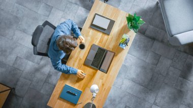 Top View shot: İşadamı İçişleri Bakanlığındaki bir dizüstü bilgisayarla Ahşap Masa 'da oturuyor. Kahve içer, daktilo yazar, internette sörf yapar, yazılım yaratır ve dizayn eder, çevrimiçi alışveriş yapar.