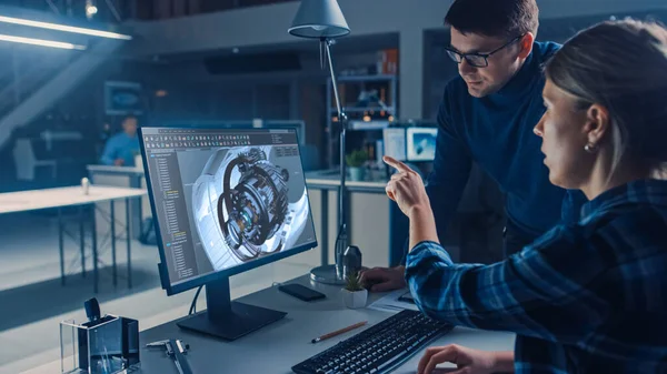 Ingeniera que trabaja en la computadora de escritorio, pantalla que muestra el software del CAD con el modelo 3D del motor, su encargado masculino del proyecto explica las especificaciones del trabajo. Oficina de Ingeniería de Diseño Industrial — Foto de Stock