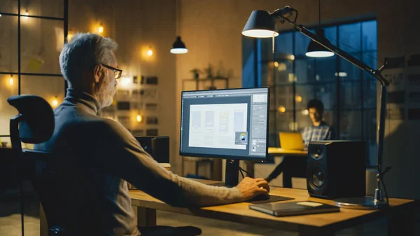 Kreativer mittelalter mobiler Software-Designer, der an seinem Schreibtisch sitzt, verwendet Desktop-Computer mit Bildschirm, der Smartphone-Anwendungsentwurfsprozess zeigt. Stilvolles modernes Studio-Büro — Stockfoto