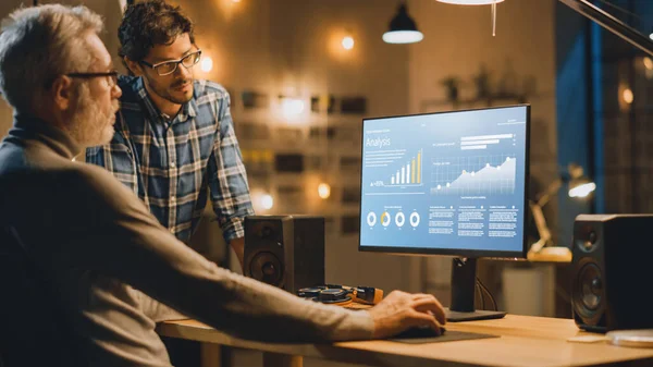 Profesyonel Üst Düzey İş Analisti Masaüstü Bilgisayarında Çizelgeler, Grafikler ve Ona Tavsiye Veren Genç Uzmanla Sohbet Ediyor. Akşamları Modern İş Ofisi