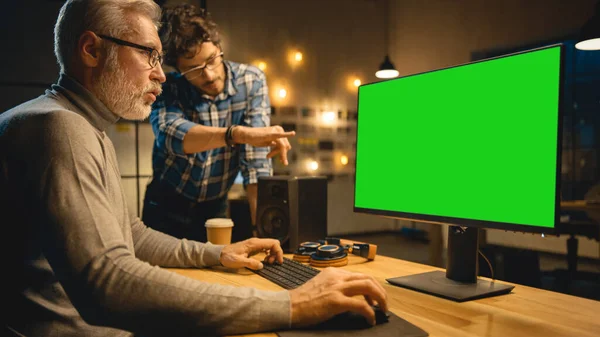 Dans la soirée créative Moyen Age Homme travaille sur un ordinateur de bureau Green Mock-up écran, a une conversation avec le jeune spécialiste qui utilise Tablet Computer. Bureau élégant Big City tard dans la soirée — Photo