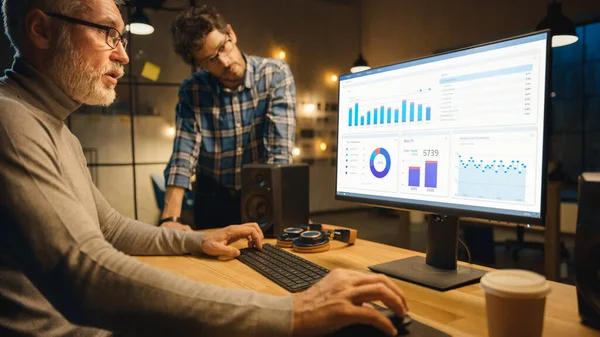 Profesyonel Üst Düzey İş Analisti Masaüstü Bilgisayarında Çizelgeler, Grafikler ve Ona Tavsiye Veren Genç Uzmanla Sohbet Ediyor. Akşamları Modern İş Ofisi