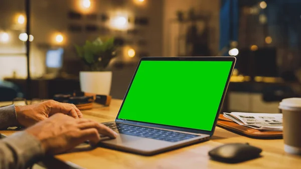 Närbild On the Hands of the Male Specialist fungerar på en bärbar dator med Mock-up grön skärm. I bakgrunden kväll i den eleganta Studio Office — Stockfoto