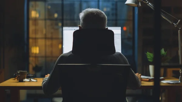 Vue arrière Vue de l'homme d'affaires assis à son bureau à l'aide d'un ordinateur de bureau. Studio de bureau élégant avec lumière tamisée et vue sur la grande fenêtre du paysage urbain — Photo