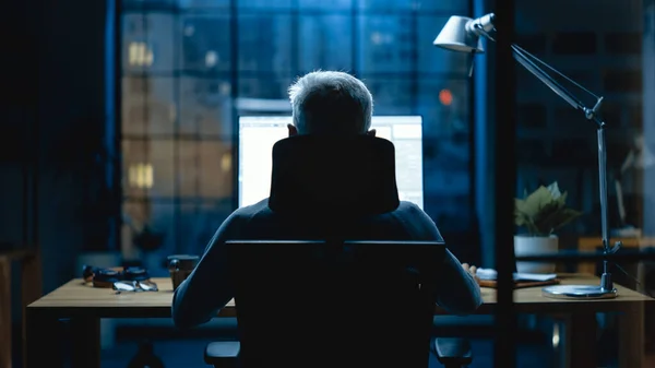 Vue arrière Vue de l'homme d'affaires assis à son bureau à l'aide d'un ordinateur de bureau. Studio de bureau élégant avec lumière tamisée et vue sur la grande fenêtre du paysage urbain — Photo