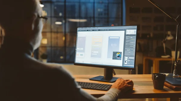 Sobre el hombro de un desarrollador de aplicaciones de mediana edad confiado usando computadora de escritorio, creando un nuevo diseño de aplicación de teléfono móvil, desarrollo de interfaz de usuario de software. Noche en Oficina con Vista a la Ventana de la Ciudad —  Fotos de Stock