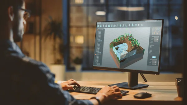 Az Esti Kreatív Fiatal Videojáték Fejlesztő Asztali Számítógépen dolgozik képernyős 3D Videojáték szintű tervezéssel. Stílusos Creative Studio Office. A válllövésen túl. — Stock Fotó