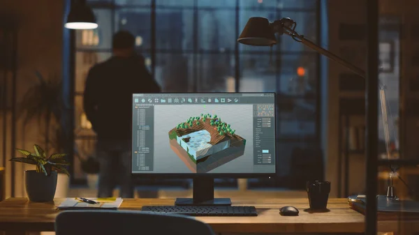 Aufnahme eines Desktop-Computers mit 3D-Videospielentwicklungssoftware im modernen Büro. Im Hintergrund blickt Designer Drinks aus einer Tasse aus dem Fenster auf die nächtliche Stadt. — Stockfoto