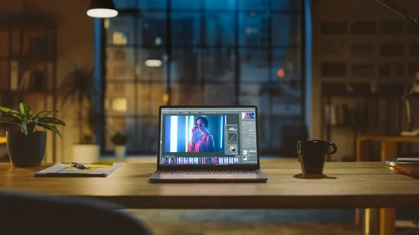 Prise de vue d'un ordinateur portable dans le bureau moderne montrant le logiciel d'édition de photos. En arrière-plan Éclairage du soir chaud et studio à espace ouvert avec vue sur la fenêtre de la ville — Photo