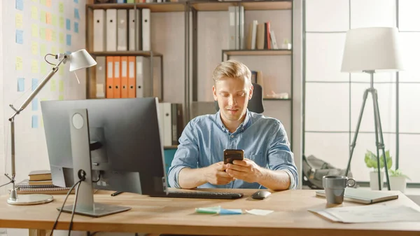 Entrepreneur créatif assis à son bureau travaille sur ordinateur de bureau dans le bureau élégant, ramasse et commence à utiliser Smartphone, Utilise l'application de médias sociaux, Emailing partenaires d'affaires, Messagerie amis — Photo