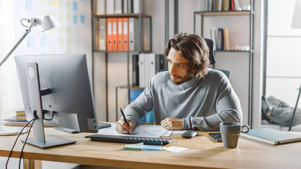 Yakışıklı Uzun Saçlı Girişimci Ofis 'teki Masasında Masaüstü Bilgisayarında Çalışıyor, Belgelerle Çalışıyor, Çizelgeleri Düzeltiyor, Grafikler Çiziyor, İstatistik ve Güncelleme Şirketi Stratejisi