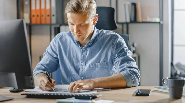 Όμορφος Blonde Businessman κάθεται στο γραφείο του στο γραφείο λειτουργεί σε επιτραπέζιο υπολογιστή, που εργάζονται με έγγραφα, διαγράμματα, γραφικές παραστάσεις, στατιστικό και στρατηγική. Δημιουργικός επιχειρηματίας χρησιμοποιώντας υπολογιστή — Φωτογραφία Αρχείου