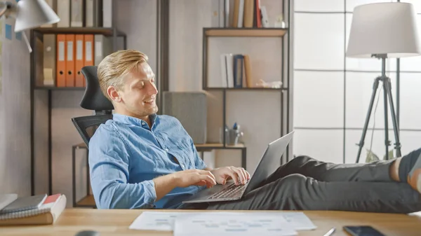 Przystojny młody przedsiębiorca pracuje na laptopie z nogami na biurku. Projektant używa notebooka do tworzenia oprogramowania Unicorn Startup. Papier do pisania Chill Student dla Uniwersytetu — Zdjęcie stockowe