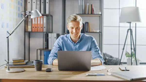 Creative Entrepreneur Sitting at His Desk Works on a Laptop in the Stylish Office, Uses Software for Social Media Apps, Emailing Business Associates, Reading News, Browsing through Internet