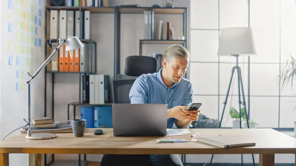 Επιχειρηματίας κάθεται στο γραφείο του λειτουργεί σε επιτραπέζιο υπολογιστή στο κομψό γραφείο, ελέγχει Smartphone του, Social Media App, e-mail Business Associates, Μηνύματα — Φωτογραφία Αρχείου