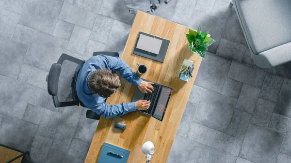 Top View Shot: Zakenman Zittend aan de Wooden Desk Works op een laptop in zijn kantoor. Hij typt, schrijft, surft op het internet, maakt en ontwerpt software, online winkelen — Stockfoto