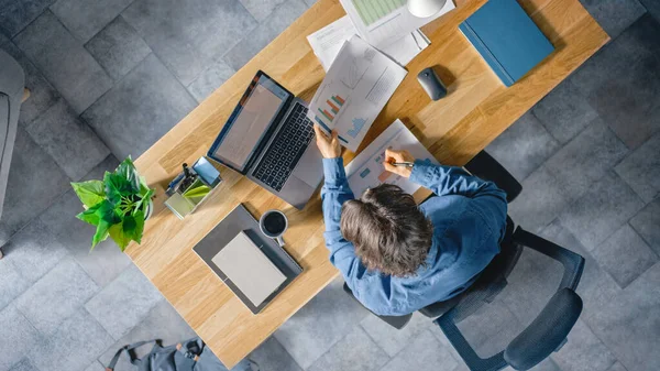 Ofisteki Masasında Oturan İşadamı Dizüstü bilgisayar kullanıyor, Şirket Strateji Belgeleri, Çizelgeler, Çizimler ve İstatistikler ile çalışıyor. Üst Görünüm Görüntüsü