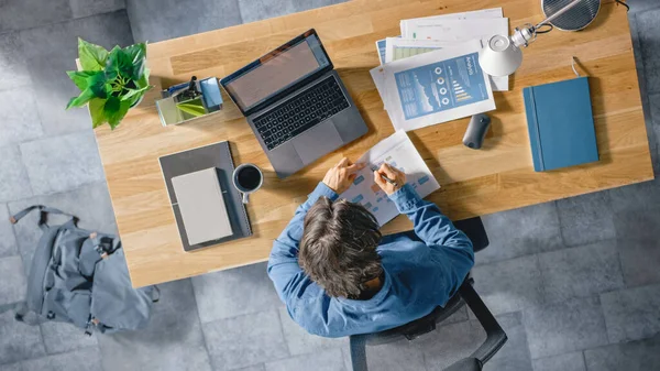 Geschäftsmann, der an seinem Schreibtisch im Büro sitzt, benutzt Laptop-Computer, arbeitet mit Unternehmensstrategien, korrigiert Diagramme, zeichnet Diagramme und Statistiken. Schuss von oben — Stockfoto