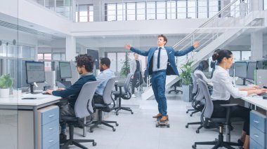 Genç Mutlu Yakışıklı Menajer Takım Elbise Giyiyor ve Uzun Tahtaya Kravat Sürüyor. Modern Açık Ofiste Çeşitli ve Motivasyonlu İş Adamları Bilgisayarlar Üzerinde Çalışıyor.