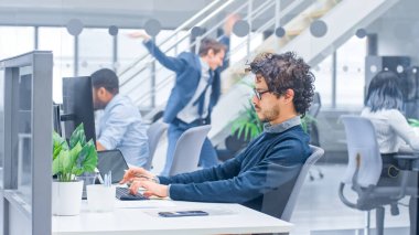 Kıvırcık Saçlı Genç Yönetici Masaüstü Bilgisayarında Çalışıyor ve Verileri Yazılımla Karşılaştırıyor. Modern Açık Ofiste Çeşitli ve Motivasyonlu İş Adamları Bilgisayarlar Üzerinde Çalışıyor.