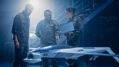 Ordu Havacılık Mühendisleri İnsansız Hava Aracı Dronu üzerinde çalışıyor. Üniformalı Havacılık Uzmanları konuşuyor, dizüstü bilgisayar kullanıyor. Gözetleme, Savaş Taktikleri, Hava Saldırıları için Uçaklı Sanayi Tesisi