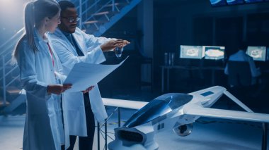 İki Uzay Mühendisi İnsansız Hava Aracı Drone Prototipi üzerinde çalışıyor. Havacılık bilimcileri planlar kullanarak konuşuyor. Ticari Hava Gözetleme Uçakları Endüstriyel Laboratuvarı