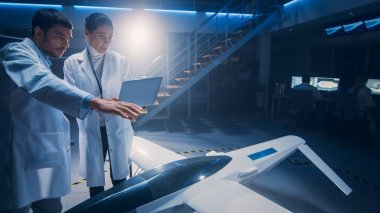 İnsansız Hava Aracı Drone Prototipi üzerinde çalışan Uzay Mühendisleri Toplantısı. Beyaz önlüklü havacılık bilimcileri konuşuyor. Endüstriyel Laboratuvarda Ticari Hava Gözetleme Uçağı