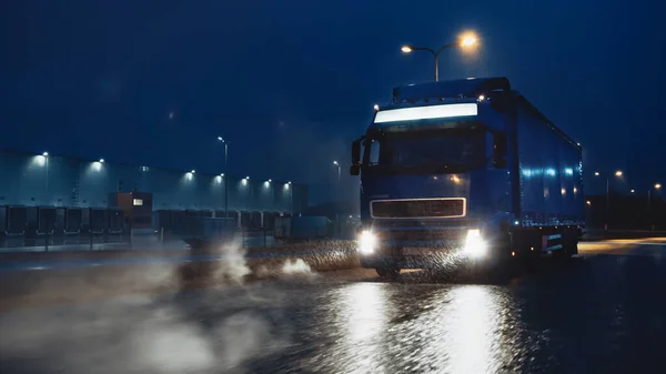 Blue Long Haul Semi-Truck mit Frachtanhänger voller Güter reist nachts auf der Freeway Road durch Regen, Nebel und Schnee quer durch den Kontinent. Bereich Industriehallen. — Stockfoto