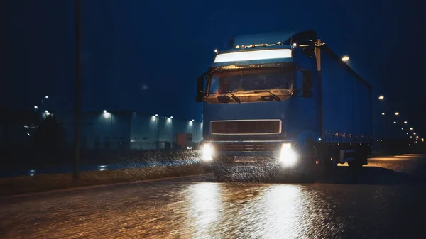 Blue Long Haul Semi-Truck with Cargo Trailer Full of Goods Travels At Night on the Freeway Road, Driving Across Continent Through Rain, Fog, Snow. Industrial Warehouses Area. — Stock Photo, Image