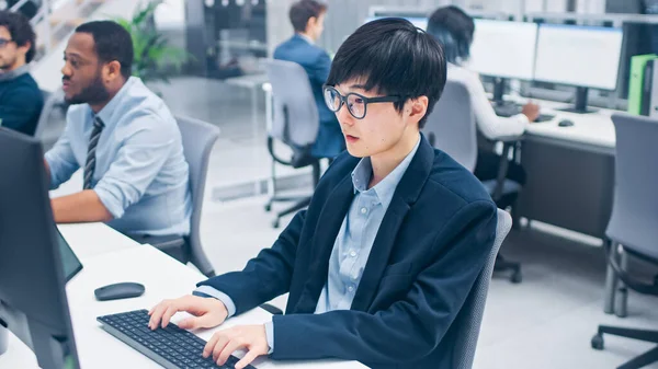 Młody profesjonalny japoński makler giełdowy Praca na komputerze stacjonarnym. Zróżnicowani i zmotywowani ludzie biznesu pracują w nowoczesnym otwartym biurze. — Zdjęcie stockowe