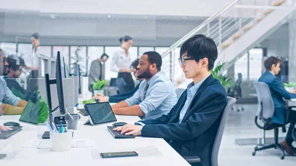 Die Aufnahme eines jungen japanischen Wirtschaftsspezialisten arbeitet auf Desktop-Computern. Vielfältiges Team junger und motivierter Unternehmer in modernem Open Office. — Stockfoto