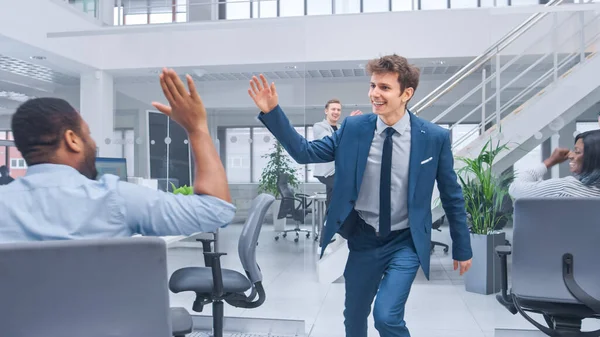 Junger glücklicher Unternehmensmanager in Anzug und Krawatte tanzt und gibt High Fives im Büro. Erfolg feiern. Vielfältige und motivierte Geschäftsleute arbeiten im modernen Open Office an Computern. — Stockfoto