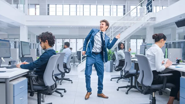 Ung glad stilig affärschef bär kostym och slips dans på kontoret. Mångfaldiga och motiverade affärsmän arbetar med datorer i moderna öppna kontor. — Stockfoto