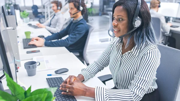 Smukke unge kvindelige kundeservice operatør arbejder i en travl moderne Call Center med Diverse multikulturelle Team af Office specialister iført headsets og tager opkald. - Stock-foto