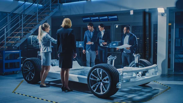 Equipo Diverso de Ingenieros de Diseño de Automóviles Presentando Chasis de Plataforma de Coche Eléctrico Autónomo Futurista a un Grupo de Inversores y Empresarios. Marco del vehículo con ruedas, motor y batería —  Fotos de Stock