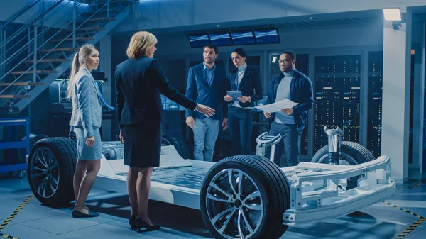 自動車設計技術者の国際チームは、投資家やビジネスマンのグループに未来的な自律型電気自動車プラットフォームシャーシを紹介します。ホイール、エンジン、バッテリー付き車両フレーム — ストック写真
