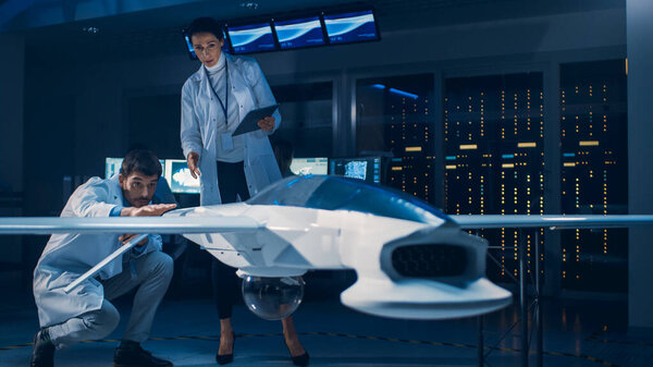 Meeting of Aerospace Engineers Working On Unmanned Aerial Vehicle Drone Prototype. Aviation Scientists in White Coats Talking. Commercial Aerial Surveillance Aircraft in Industrial Laboratory